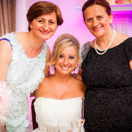 Bride smiling with two women in elegant attire, celebrating at a wedding reception, capturing candid joy and connection.