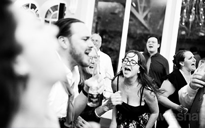 Candid moment of wedding guests joyfully singing and celebrating, showcasing authentic emotions and energy in a lively event atmosphere.