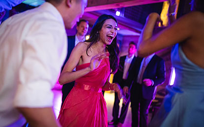 Woman in a vibrant pink dress laughing and dancing joyfully at a lively event, surrounded by elegantly dressed guests, capturing the authentic energy and candid moments of celebration.