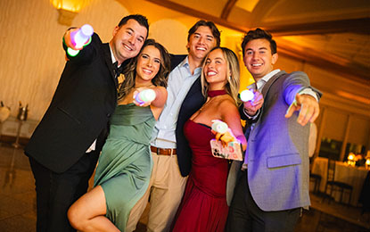 Group of five friends celebrating at a wedding reception, smiling and posing with colorful light-up party favors, capturing the lively atmosphere and authentic moments of the event.