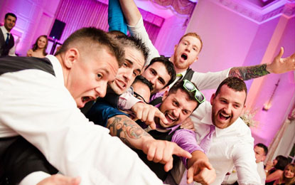 Group of men celebrating at a wedding reception, expressing joy and excitement, with vibrant lighting and a lively atmosphere, capturing authentic moments of connection and fun.