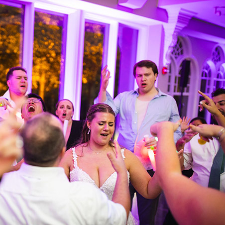 Bride dancing joyfully with guests at a wedding reception, vibrant lighting, capturing the energy and authentic moments of celebration.