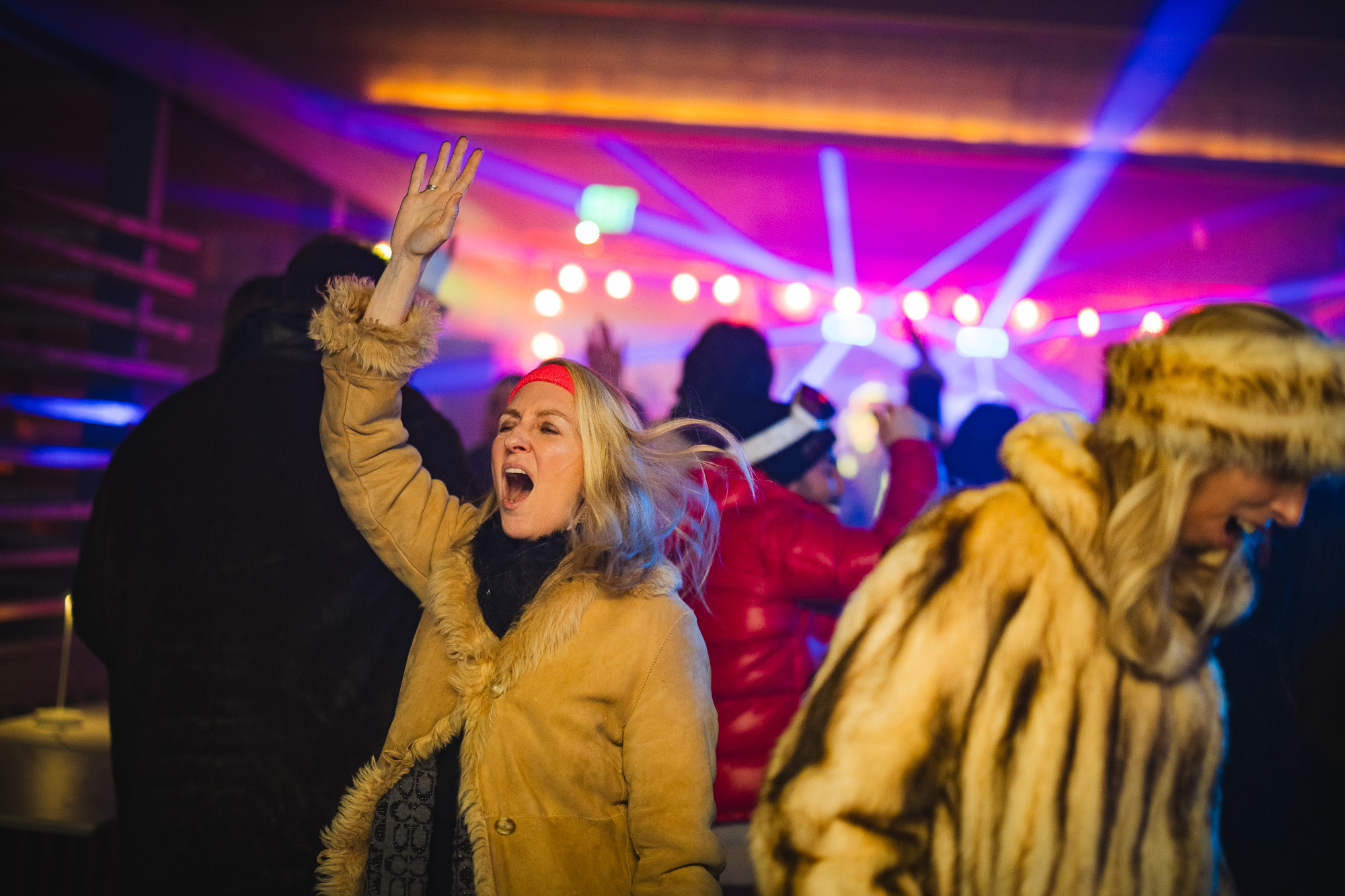 Woman dancing joyfully in 80's ski chic attire at Après Ski winter event, vibrant atmosphere with colorful lights and lively crowd at The Bridge At Saugatuck.