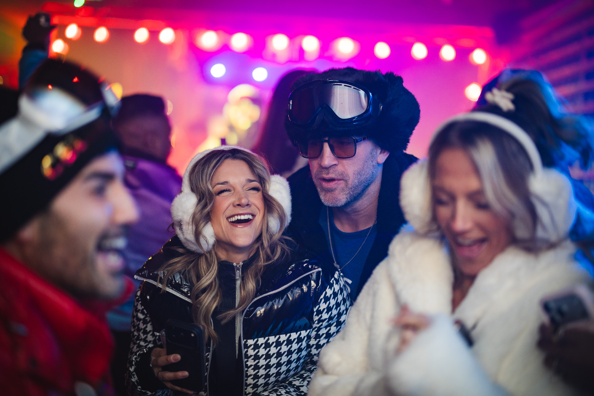 Group of friends enjoying the Après Ski winter event at The Bridge At Saugatuck, dressed in 80's ski chic attire, with vibrant lighting and laughter capturing the festive atmosphere.