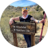 Image of a smiling woman standing next to a hiking trail sign, showcasing a vibrant outdoor setting, reflecting the authentic moments captured by Awesnap photography services.